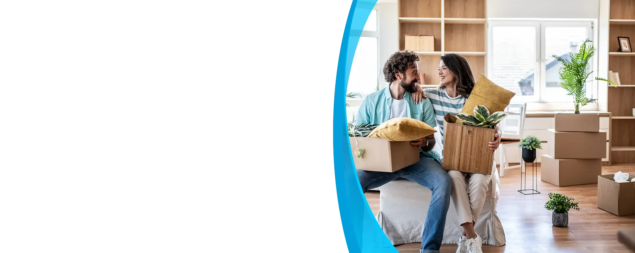 A smiling couple sits among moving boxes and houseplants in their bright new living room.